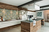 A modern, open-plan kitchen with Mediterranean-style wall tiles and an island counter clad with raw wood