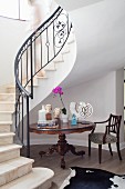 Sculptures on Baroque table at foot of elegantly winding staircase in foyer