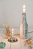 Festive arrangement of origami candlestick and bottle covered in newspaper on table