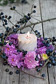 Candle in autumnal wreath of pompom dahlias, hydrangea flowers and sloe branches