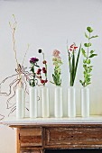 Row of white vases holding single flowers on vintage cabinet