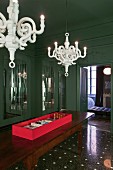 Modern white chandeliers in dark green room with coffered walls and terazzo floor