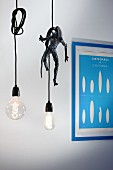 Two purist pendant lamps with illuminated light bulbs and knotted cables, one with Alien figurine