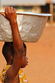 Kind trägt Wasserschüssel auf dem Kopf in einem afrikanischen Dorf, Togo, Westafrika