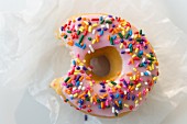 A doughnut decorated with sugar sprinkles, with a bite taken out (seen from above)