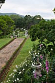Weg mit Natursteinbelag und weiße Rankbögen in weitläufigem Garten