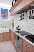 L-shaped kitchen counter in pale wood with marble counter and mantel hood over cooker