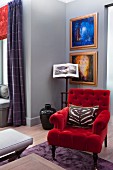 Armchair with red velvet cover in front of gilt-framed artworks on grey-painted wall