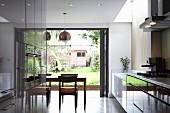 Offene Küche mit glänzender Schrankfront und Essbereich vor Terrassenfalttür
