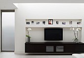 Low, black sideboard and flatscreen TV in niche in contemporary living room