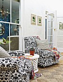 Two black and white floral armchairs in front of lattice window with view into living room