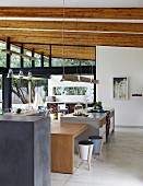 Solid wooden dining table adjoining kitchen counter in open-plan kitchen with rustic wood-beamed ceiling