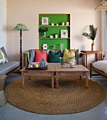 Wooden tables on round sisal rug in front of cushions on bench and ornaments in green-painted niche