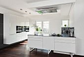 A white, open-plan designer kitchen with an island counter with dark floorboards