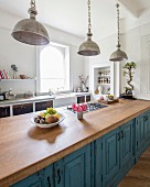 Vintage metal pendant lamps above free-standing kitchen counter with blue, patinated base units and oak worksurface