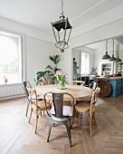 Round dining table, various chairs and lantern-style lamp with open-plan kitchen in background