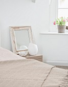 Mirror with vintage wooden frame and ornaments on bedside table, woollen blanket on bed and potted plant on windowsill