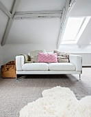 White two-seater sofa with scatter cushions and vintage wooden trunk in attic room