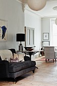 Black, antique armchair next to bistro table and seating area in background in traditional living room