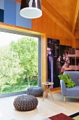 Grey crocheted pouffes and modern side table in front of large window with view of garden