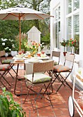 Outdoor wicker chairs at a a table laid under a parasol