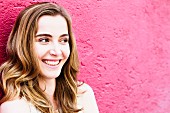 Portrait von dunkelblonder Frau vor pinkfarbener Mauer