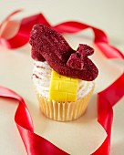 A Wizard of Oz themed cupcake decorated with a red shoe and a yellow brick road