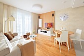 Dining set with white chairs at wooden table and pale sofa in open-plan, modern interior