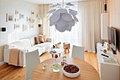 Designer pendant lamp with white leaves above round dining table and pale sofa in background in modern interior