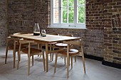 Dining area with classic chairs around wooden table in loft interior with rustic brick wall