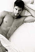 A young, topless man lying on a bed (black-and-white photo)