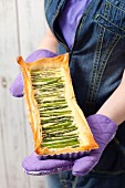 A woman holding a puff pastry tart with asparagus