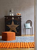 Orange pouffe and rug in front of ethnic-style chest of drawers and chair