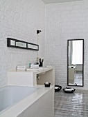 Fitted bathtub, masonry washstand and full-length mirror against whitewashed brick walls