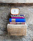Alarm clock and stacked books on vintage stone bracket on stone wall