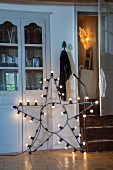 Star-shaped lamp with light bulbs on wire frame leaning against fitted cupboard in rustic interior