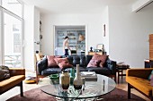 Round glass table, armchairs and leather couch in open-plan interior