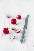 Radishes (whole and halved) on a white wooden surface with a knife