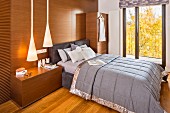 Double bed with grey bedspread against wood-clad wall with integrated cabinets