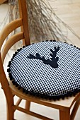 Round cushion made from blue and white gingham cotton decorated with pompom trim and stag's head appliqué