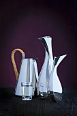 Curved silver-plated designer jugs and a glass of water