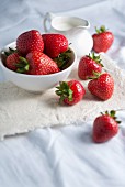 Fresh strawberries in a bowl with a jug of cream on a linen cloth