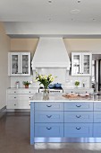 Kücheninsel mit blauen Schubladen und Marmor Arbeitsfläche in eleganter Landhausküche, im Hintergrund Dunstabzug in Weiß über Küchenzeile