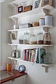 White bracket shelves of storage jars and cookery books in corner of kitchen