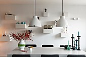 Industrial-style pendant lamps above branches of berries in vase of candlesticks on dining table in front of ornaments on small bracket shelves
