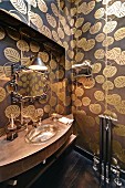 Badezimmer mit geschwungenem Waschtisch, eingebautem Silberbecken, Wandtapete mit goldenen Blattmotiven und Spiegel mit Vintage-Rahmen