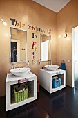 White, twin washstands with countertop basins, mirrors and motto painted on apricot wall
