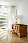 Table lamp with white lampshade on antique, carved wooden cabinet in corner of living room with marble floor