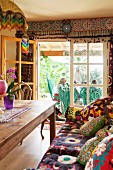 Gemütliches Wohnzimmer im Ethno-Stil, Bank mit verschiedenen bunt gemusterten Textilien, Blick durch offene Terrassentür