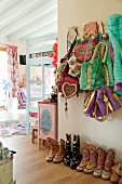 Pastellfarbenes Kinderzimmer im Folklore-Stil, Sammlung bunter Cowboystiefel und Garderobe mit verschiedenen Taschen